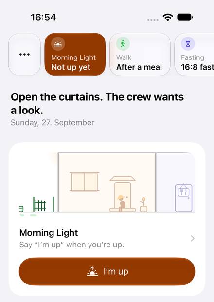 The Today screen. At the top, a strip of glass chips: a menu, Morning Light “Not up yet” highlighted in orange, Walk “After a meal”, Fasting “16:8 fast”. Below: “Open the curtains. The crew wants a look.” and the date. A card peeks into the porch, where a crew member sits on the step by the door, above the words “Say ‘I’m up’ when you’re up.” and an I’m up button.